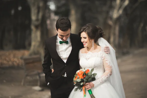 Прекрасная счастливая свадебная пара, прогуливающаяся по парку в свой день с букетом — стоковое фото