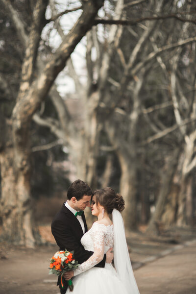 Beautiful happy wedding couple walking in the park on their day with bouquet