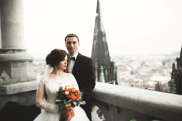 Hermosa pareja de recién casados de pie en el balcón con una vista de la ciudad — Foto de Stock