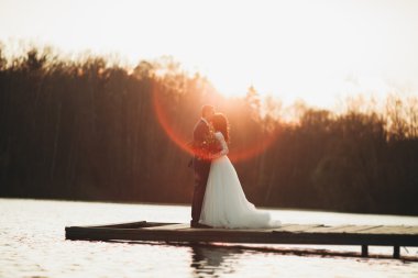 Zarif güzel düğün çifti bir göl kenarında günbatımında poz