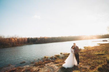 Zarif güzel düğün çifti bir göl kenarında günbatımında poz