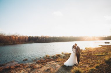 Zarif güzel düğün çifti bir göl kenarında günbatımında poz