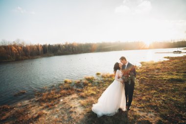 Zarif güzel düğün çifti bir göl kenarında günbatımında poz