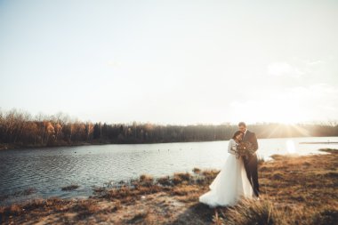 Zarif güzel düğün çifti bir göl kenarında günbatımında poz