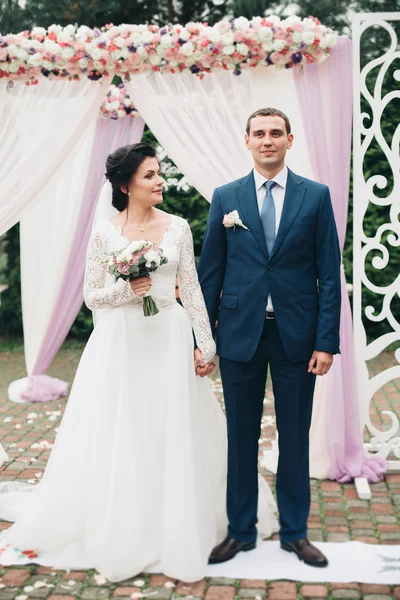 Casamento casal de pé sob um arco de flores frescas — Fotografia de Stock