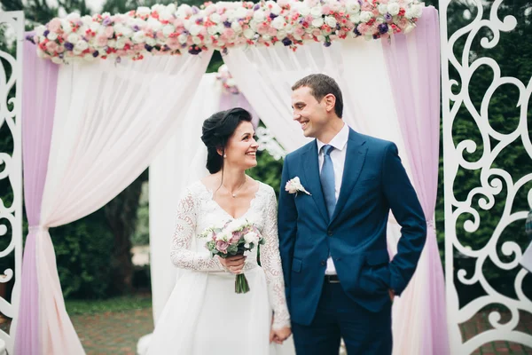 Paar staande onder een boog van verse bloemen bruiloft — Stockfoto
