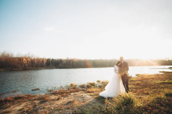 Zarif güzel düğün çifti bir göl kenarında günbatımında poz — Stok fotoğraf