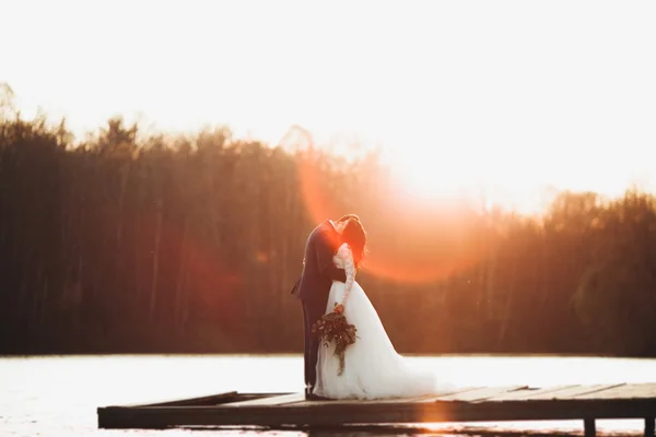 Elegante mooie bruidspaar poseren in de buurt van een meer bij zonsondergang — Stockfoto