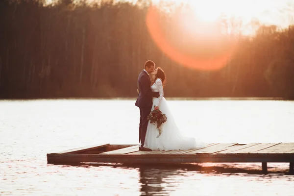 Elegante mooie bruidspaar poseren in de buurt van een meer bij zonsondergang — Stockfoto