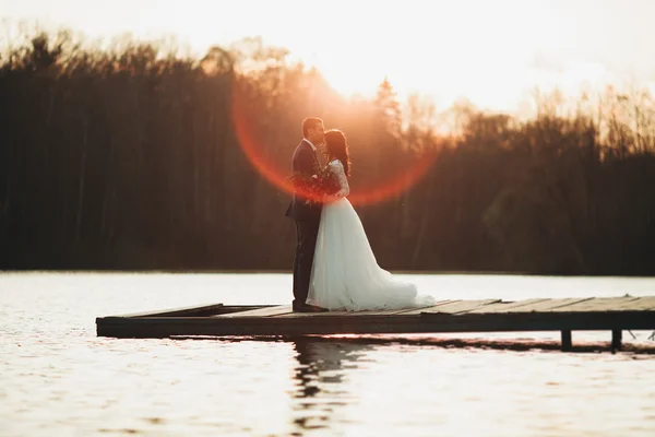 Elegante schöne Hochzeitspaar posiert in der Nähe eines Sees bei Sonnenuntergang — Stockfoto