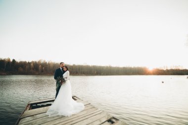 Zarif güzel düğün çifti bir göl kenarında günbatımında poz