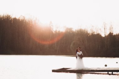 Zarif güzel düğün çifti bir göl kenarında günbatımında poz