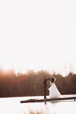 Zarif güzel düğün çifti bir göl kenarında günbatımında poz