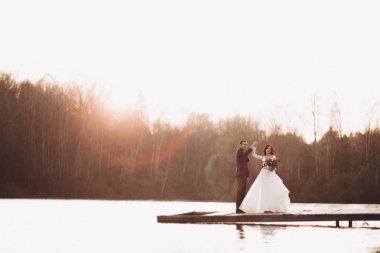 Zarif güzel düğün çifti bir göl kenarında günbatımında poz