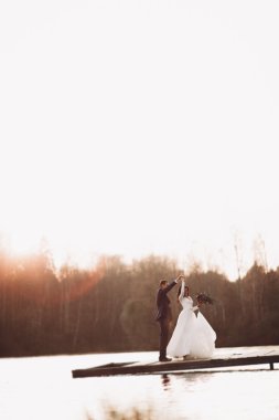 Zarif güzel düğün çifti bir göl kenarında günbatımında poz