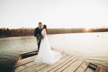 Zarif güzel düğün çifti bir göl kenarında günbatımında poz