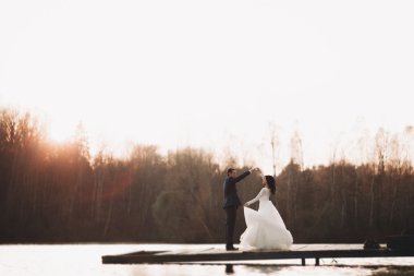 Zarif güzel düğün çifti bir göl kenarında günbatımında poz