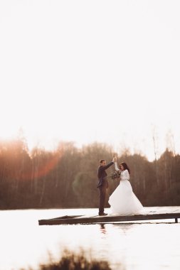 Zarif güzel düğün çifti bir göl kenarında günbatımında poz