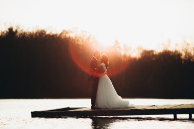 Zarif güzel düğün çifti bir göl kenarında günbatımında poz