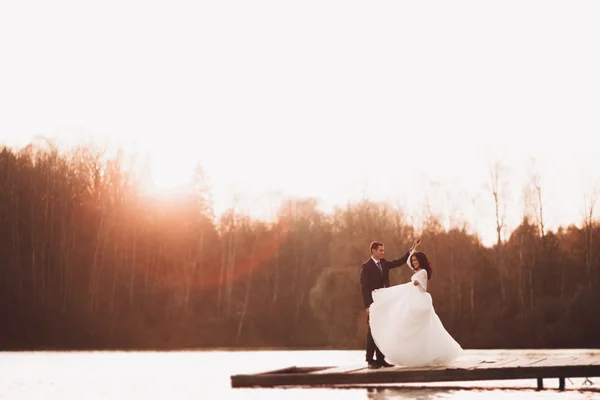 Elegante hermosa pareja de boda posando cerca de un lago al atardecer —  Fotos de Stock