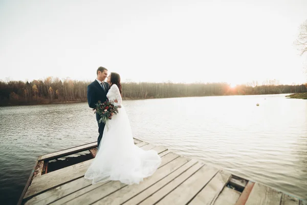 Elegante hermosa pareja de boda posando cerca de un lago al atardecer — Foto de Stock