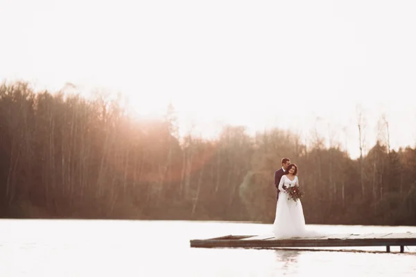 Elegante schöne Hochzeitspaar posiert in der Nähe eines Sees bei Sonnenuntergang — Stockfoto