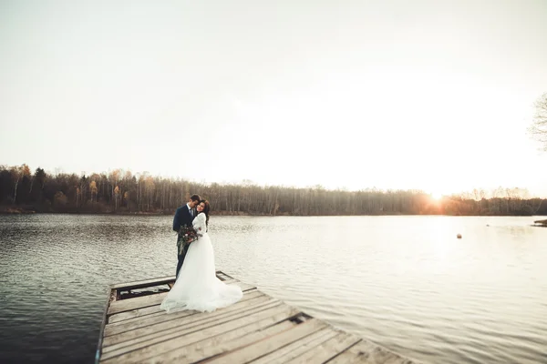 Elegante schöne Hochzeitspaar posiert in der Nähe eines Sees bei Sonnenuntergang — Stockfoto