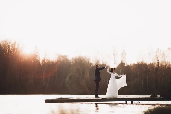 Elegante hermosa pareja de boda posando cerca de un lago al atardecer —  Fotos de Stock