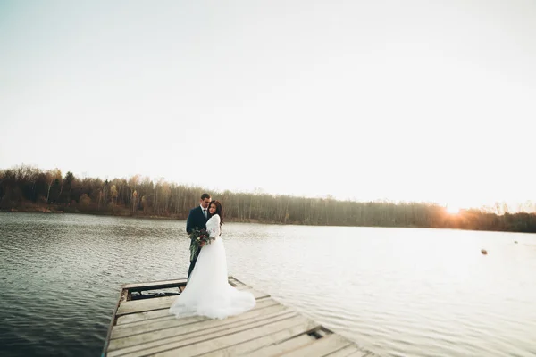 Elegante mooie bruidspaar poseren in de buurt van een meer bij zonsondergang — Stockfoto