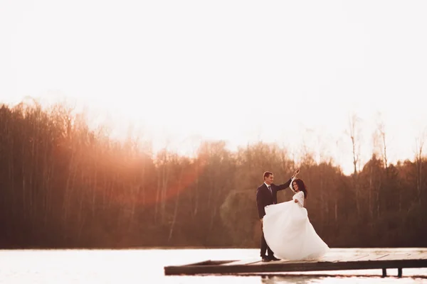 Elegante bella coppia di nozze in posa vicino a un lago al tramonto — Foto Stock