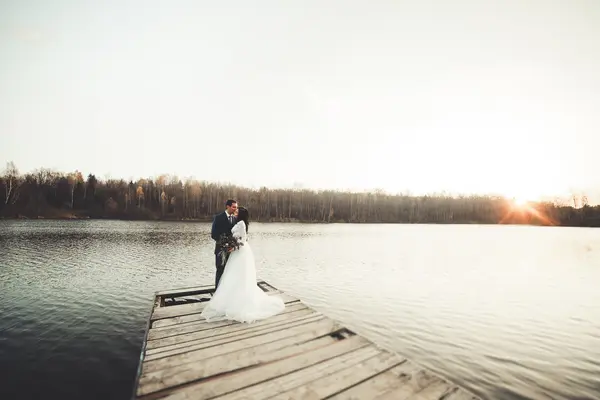 Κομψό και όμορφο γάμο ζευγάρι ποζάρει κοντά σε μια λίμνη στο ηλιοβασίλεμα — Φωτογραφία Αρχείου