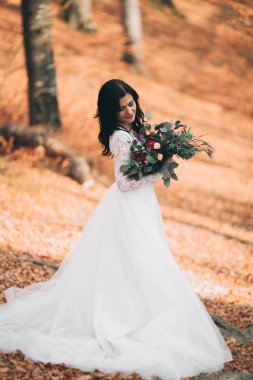Orman ve göl poz buket tutan şık elbiseli güzel esmer gelin