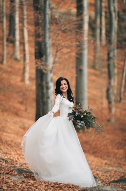 Orman ve göl poz buket tutan şık elbiseli güzel esmer gelin