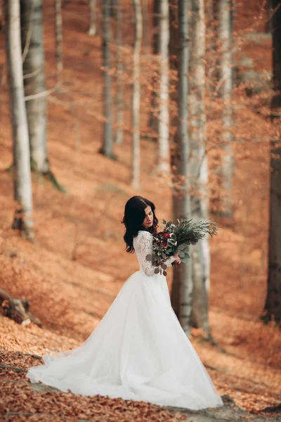 Prachtige brunette bruid in elegante jurk bedrijf boeket poseren in de buurt van bos en meer — Stockfoto