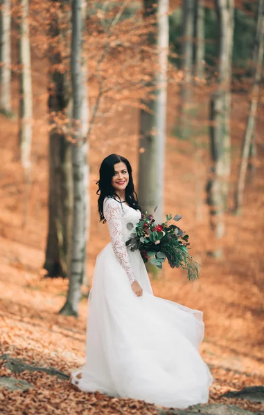 Великолепная брюнетка невеста в элегантном платье держа букет позируя возле леса и озера — стоковое фото