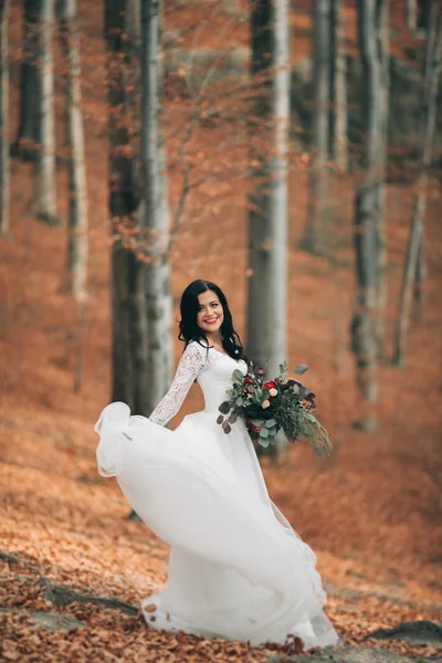 Prachtige brunette bruid in elegante jurk bedrijf boeket poseren in de buurt van bos en meer — Stockfoto