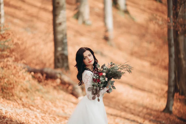 Hermosa novia morena en vestido elegante celebración de ramo posando cerca del bosque y el lago —  Fotos de Stock