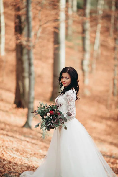 Hermosa novia morena en vestido elegante celebración de ramo posando cerca del bosque y el lago — Foto de Stock