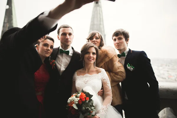 Koszorúslányok, vőfély és esküvői pár, így selfie, panorámás kilátással a városra — Stock Fotó