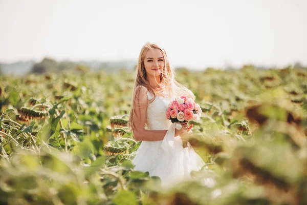 Элегантная блондинка с длинными волосами и букетом подсолнухов в поле — стоковое фото
