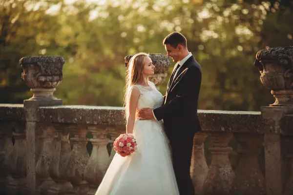 Hermosa pareja romántica de recién casados abrazándose cerca del viejo castillo en la puesta del sol —  Fotos de Stock