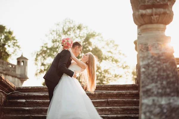 Schönes romantisches Hochzeitspaar, das sich bei Sonnenuntergang in der Nähe des alten Schlosses umarmt — Stockfoto