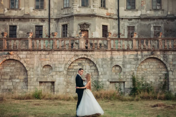 Hermosa pareja romántica de recién casados abrazándose cerca del viejo castillo en la puesta del sol —  Fotos de Stock