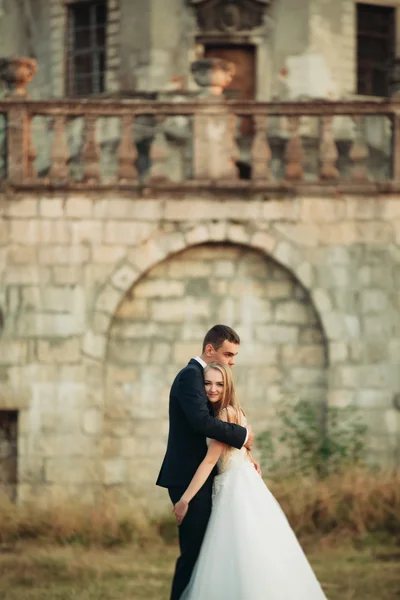 Krásné romantické svatební pár novomanželé objímání poblíž starého hradu na západ slunce — Stock fotografie