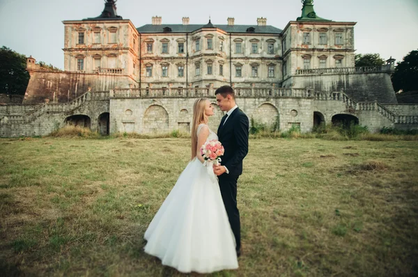 Schönes romantisches Hochzeitspaar, Bräutigam und Braut umarmen sich bei Sonnenuntergang in der Nähe des alten Schlosses — Stockfoto