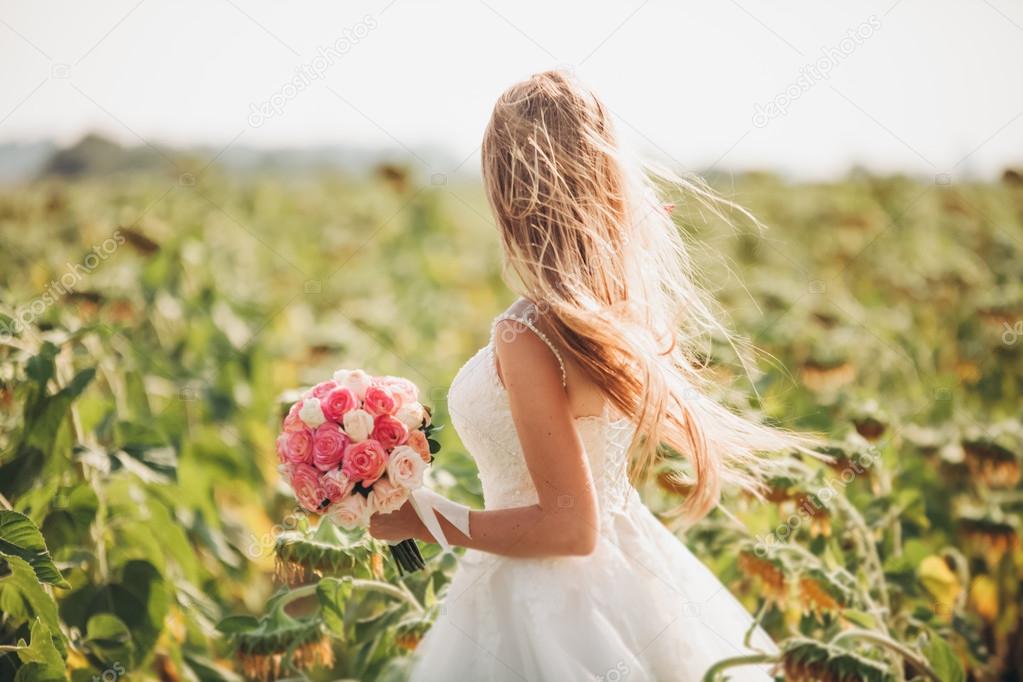 Elegant blonde bride with long hair and a bouquet of sunflowers in the field