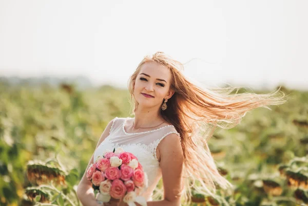Elegante blonde Braut mit langen Haaren und einem Strauß Sonnenblumen auf dem Feld — Stockfoto