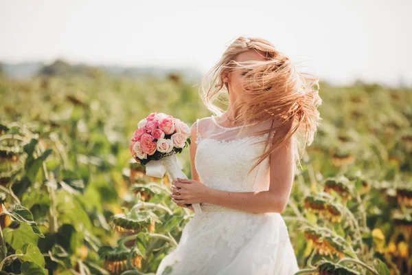 Elegante novia rubia con el pelo largo y un ramo de girasoles en el campo — Foto de Stock