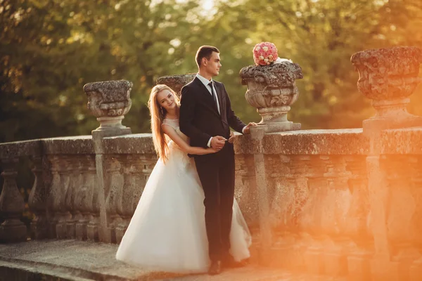 Hermosa pareja romántica de recién casados abrazándose cerca del viejo castillo en la puesta del sol —  Fotos de Stock