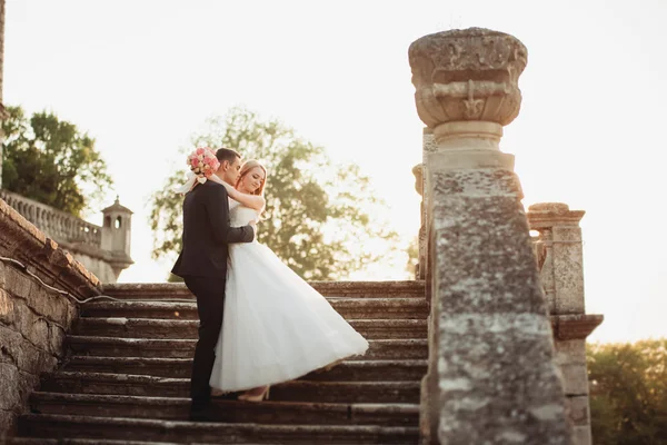 Hermosa pareja romántica de recién casados abrazándose cerca del viejo castillo en la puesta del sol — Foto de Stock